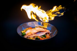 pexels-photo-11129150-11129150 Vibrant flame-grilled salmon served on vegetable fried rice, set against a striking black background.