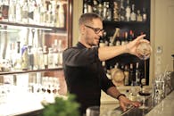 pexels-photo-3769150-3769150-1 Side view of positive young barman in black uniform and eyeglasses pouring wine into glass while working at bar counter in modern restaurant